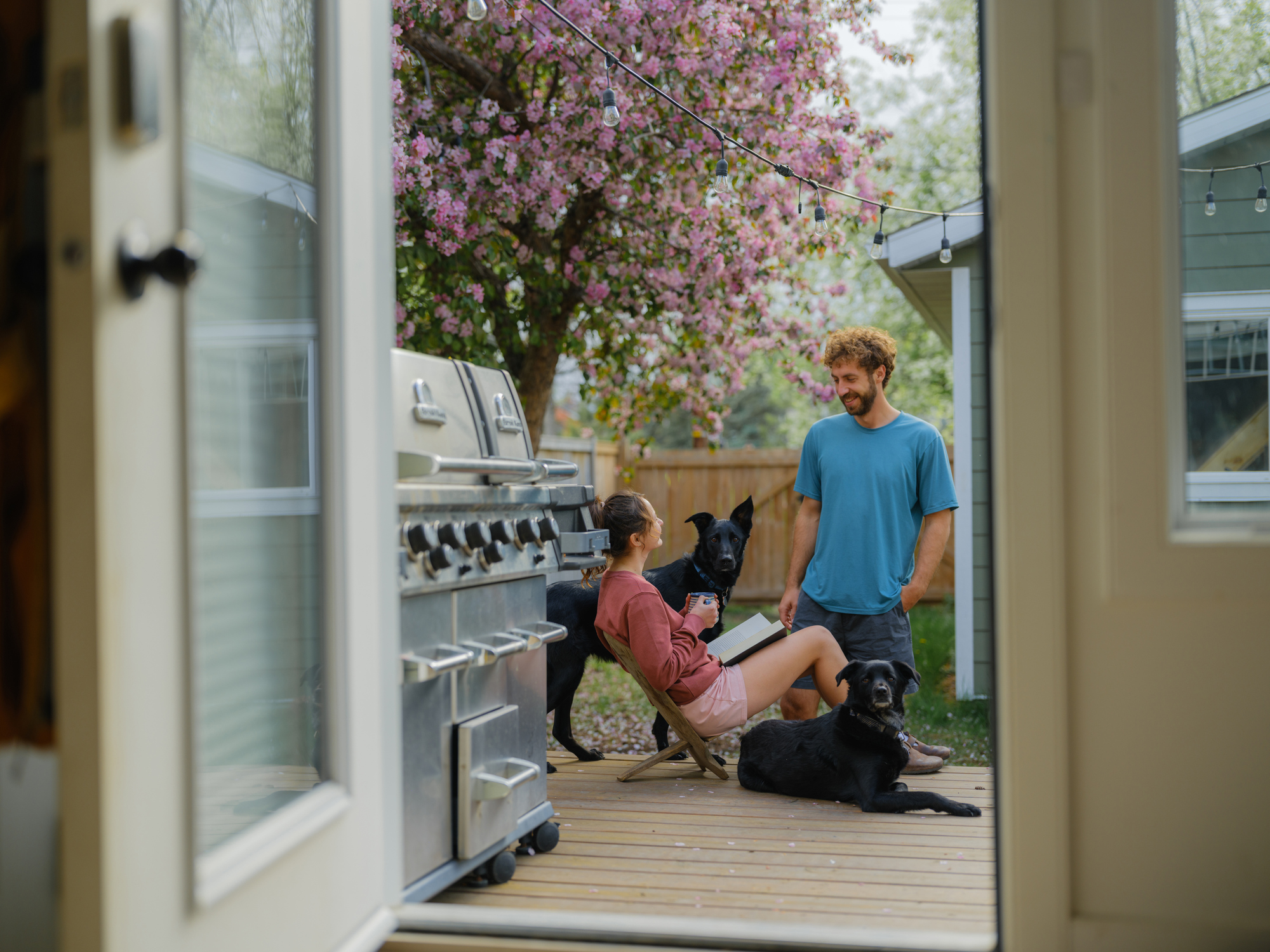 Woman reading a book sitting on the patio and drinking coffee. Sharing moment with partner and dogs.